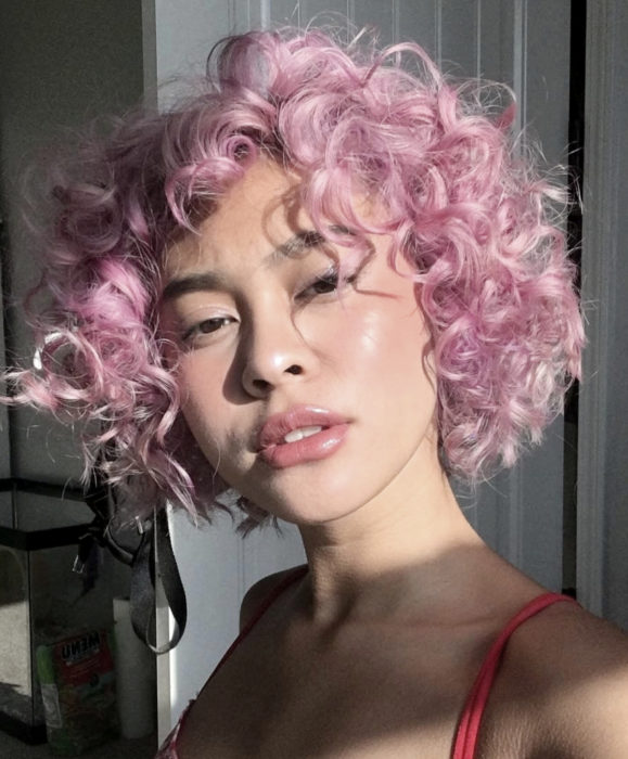 Cabello color rosa cherry blossom; mujer morena de ojos rasgados, con cabello rizado, corto y teñido