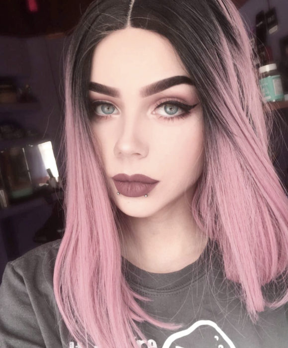 Cabello color rosa cherry blossom; chica de ojos azules, con cabello teñido y negro en las raíces, perforaciones en los labios