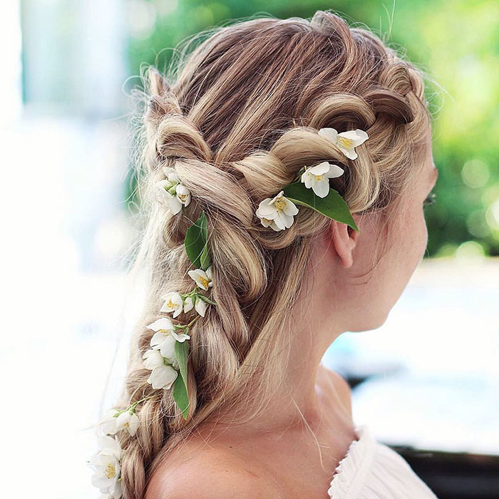 Chica rubia con trenza esponjosa con flores blancas y hojas verdes