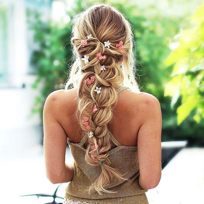 Chica rubia de cabello largo con trenza esponjosa con flores rosas