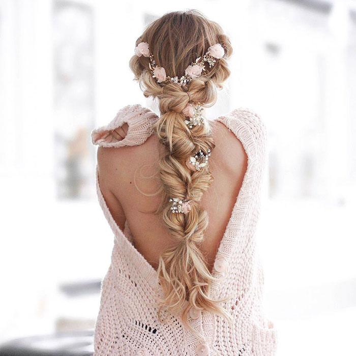 Chica rubia de cabello largo con trenza esponjosa con flores rosas