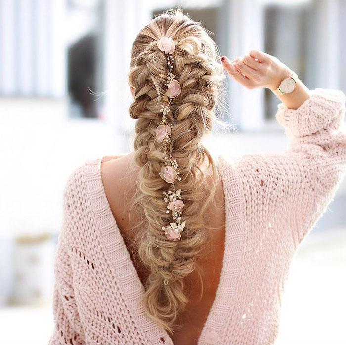 Chica rubia de cabello largo con trenza esponjosa con flores rosas