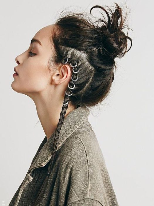 Chica posando de perfil con los ojos cerrados, peinada con bun alto y una trenza lateral con argollas