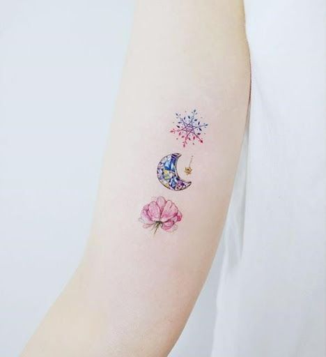 Tatuaje de copo de nieve, luna y árbol estilo acuarela en el brazo