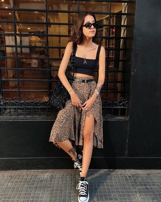 Chica posando con falda larga de animal print, crop top negro y tenis Converse