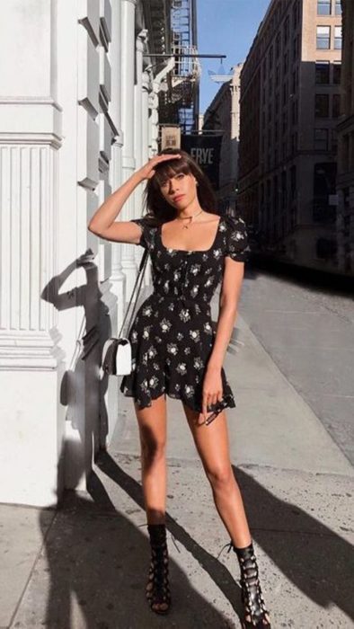 Chica cubriéndose del sol con una mano, usando un vestido de flores negro
