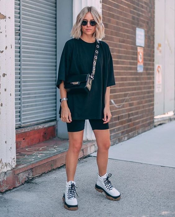 Chica rubia con cabello lacio usando blusa holgada negra con shorts negros y botas blancas