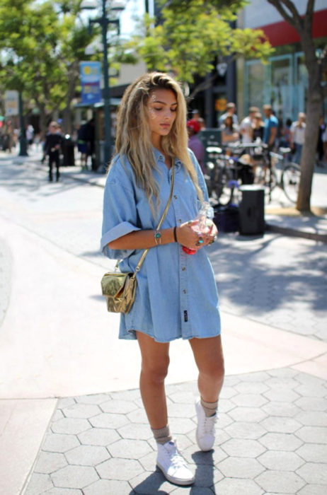 Atuendos con tu boyfriend shirt, camisa de tu novio, blusa oversized azul de mezclilla como vestido, con tenis blancos, mujer rubia en la calle