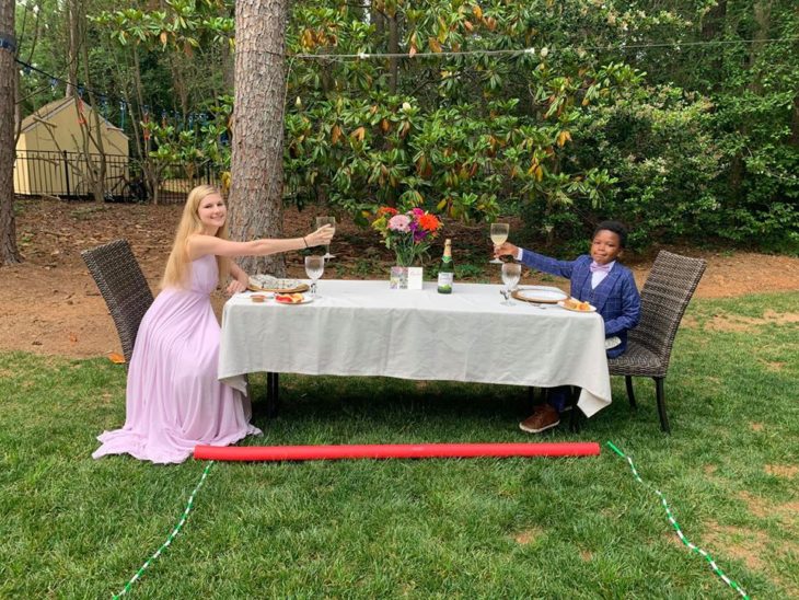 Chica y un niño disfrutando de una comida en una larga mesa de jardín con un mantel blanco