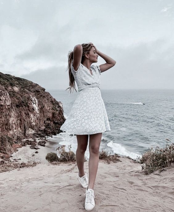Chica rubia con vestido de flores se toma el cabello mientras posa en la playa