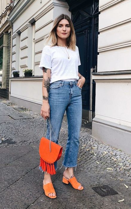 Mujer viste blusa blanca, jeans y bolsa, zapatos naranjas con tacón cuadrado