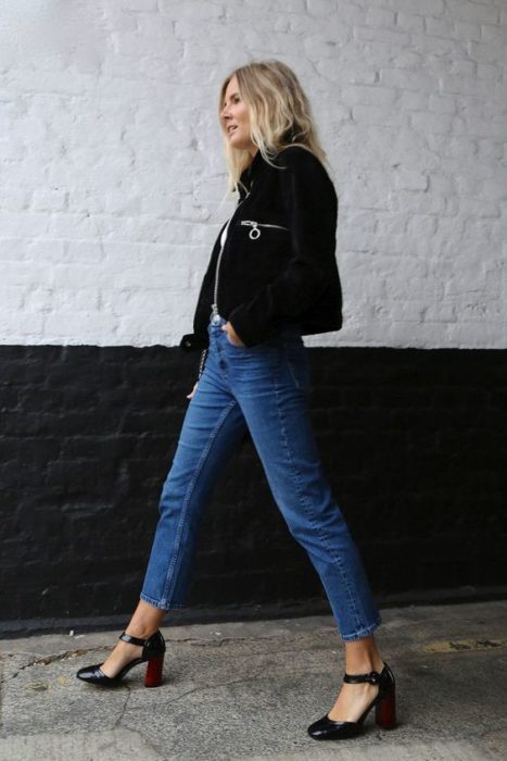 Chica rubia de cabello suelto con chaqueta negra, pantalón de mezclilla y tacones cuadrados