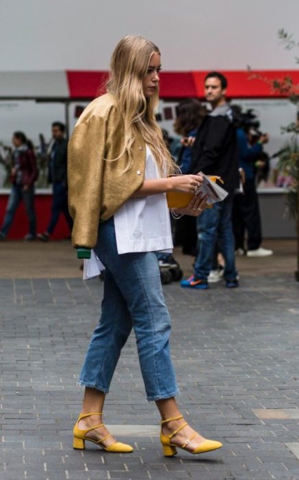 Mujer con cabello suelto viste jeans, chaqueta dorada y tacones cuadrados