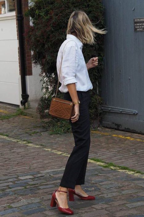 Mujer posando de espaldas, usa blusa blanca, jeans negros y tacones cuadrados