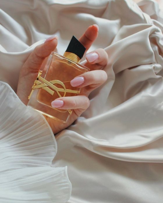 Mano de mujer sosteniendo botella de perfume en la cama
