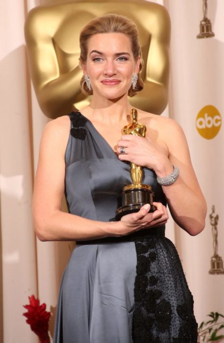 Kate Winslet con un vestido a tirantes anchos en tono gris sosteniendo una estatuilla a los premios Óscar