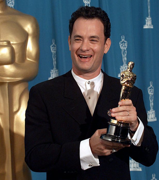 Tom Hanks sonriendo en la entrega de los premios óscar y sosteniendo una estatuilla ganadora