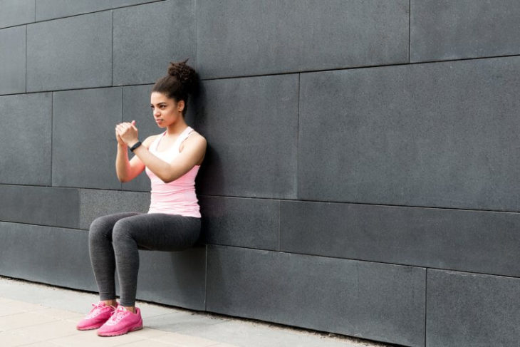 Chica realizando sentadillas apoyada en la pared