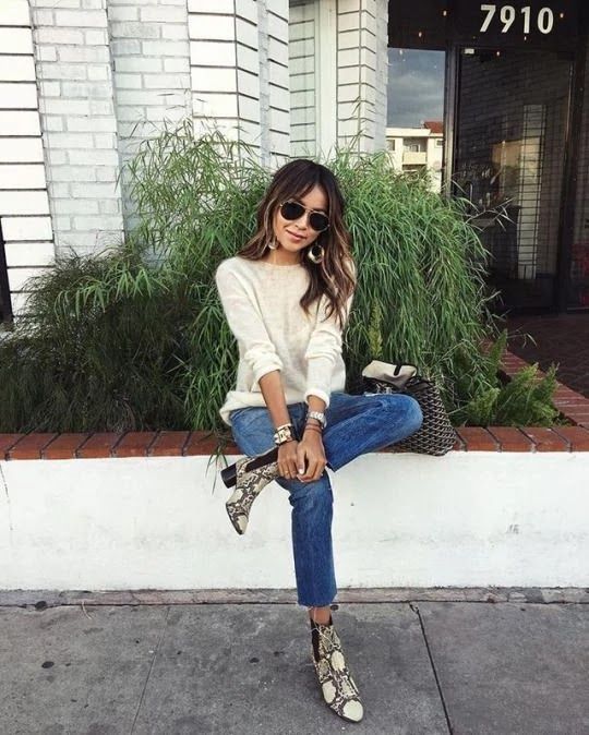 Chica morena con cabello ondulado y lentes oscuros sentada con jeans, blusa blanca y zapatos animal print