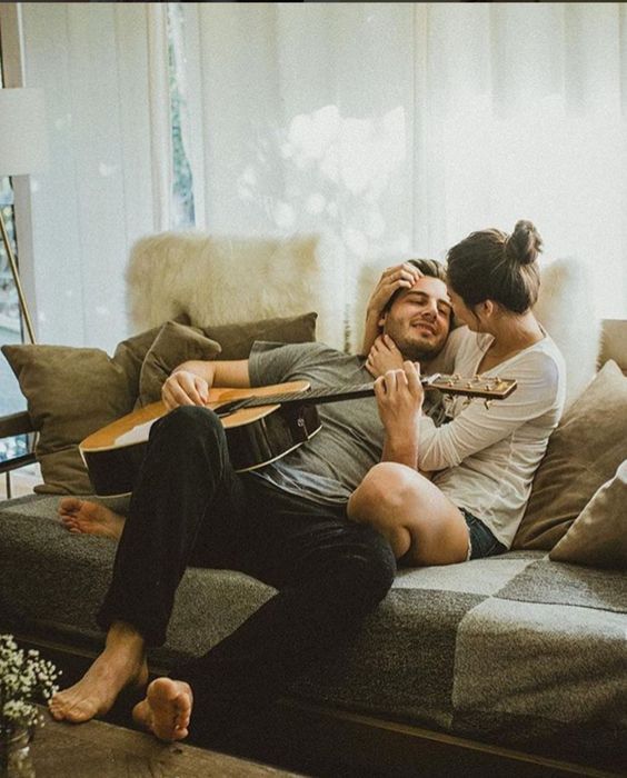 Pareja sentada en el sofá mientras él toca la guitarra