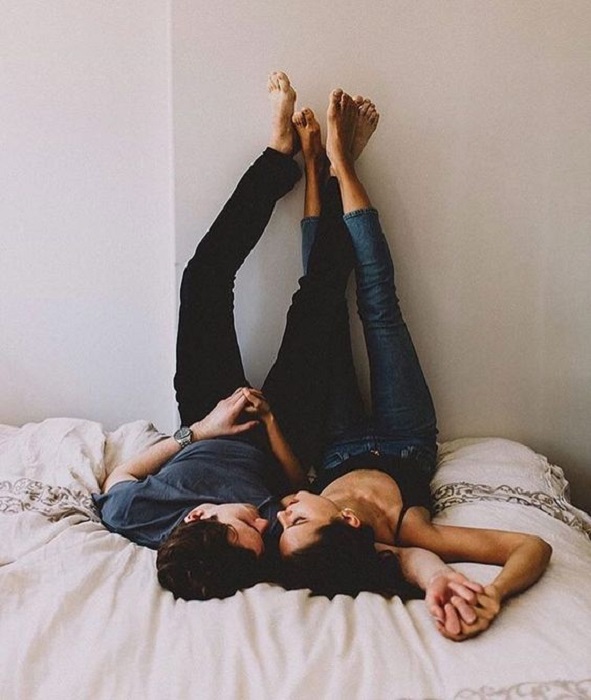 Pareja recostada con los pies sobre la pared mirándose