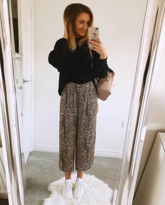 Chica rubia se toma selfie frente al espejo con suéter negro y pantalones holgados de leopardo