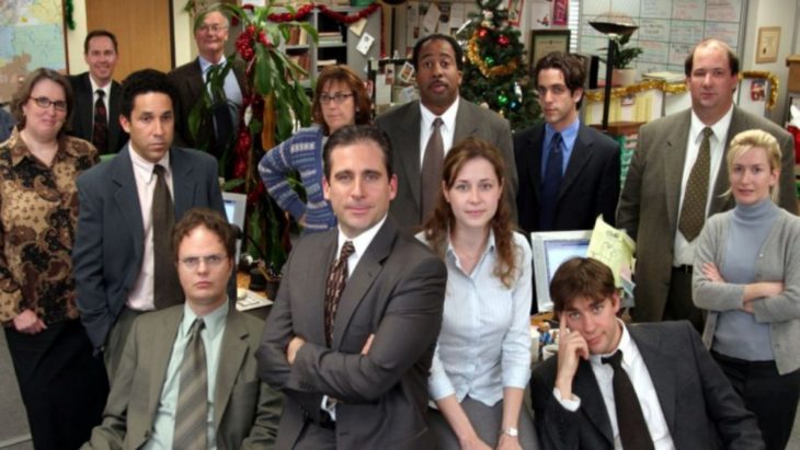 Elenco de la serie The Office sentados frente a un escritorio de madera