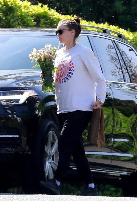 Rooney Mara con sudadera holgada bajando de una camioneta negra con un ramo de flores en la mano