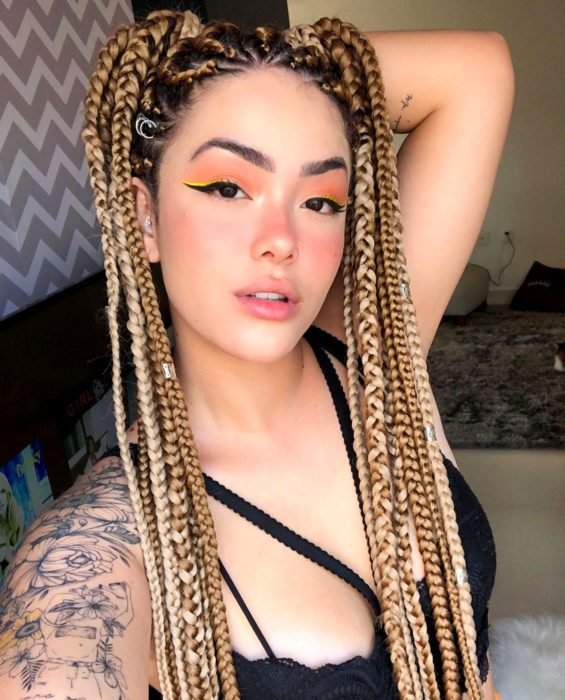 Looks con trenzas africanas; mujer de cabello largo y rubio con peinado de dos coletas altas, maquillaje natural, tatuaje de flores en el hombro