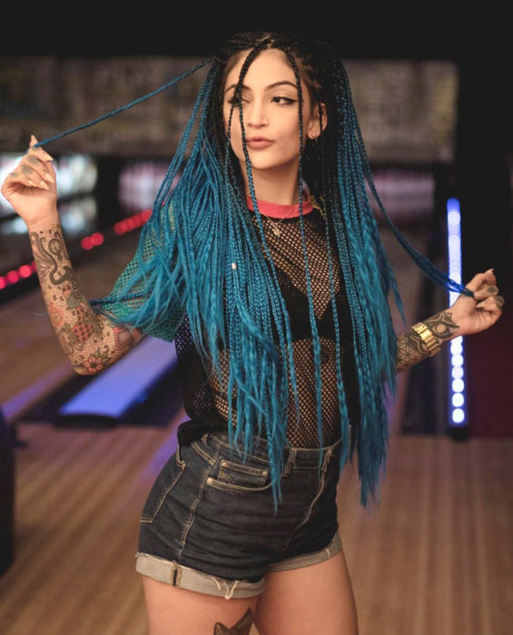 Looks con trenzas africanas; mujer de cabello largo color azul turquesa, con peinado de dos medias coletas, blusa de red y short, tatuajes en los brazos, en el boliche, Matu Garcés