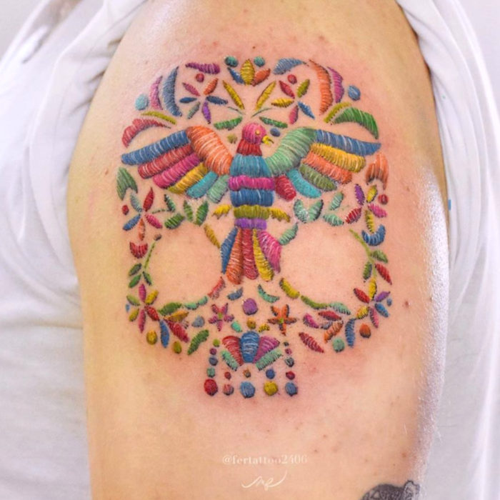 Fernanda Ramírez, tatuadora mexicana crea tatuajes bordados; pájaro de colores con calavera en el brazo