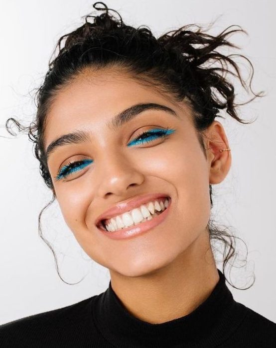 Chica morena con cabello recogido en un chongo y delineado azul en los ojos