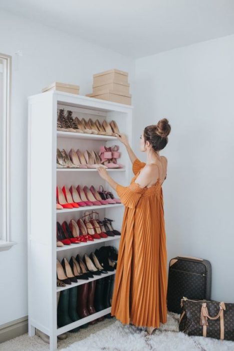 Mujer con vestido naranja acomoda zapatos en un mueble blanco 