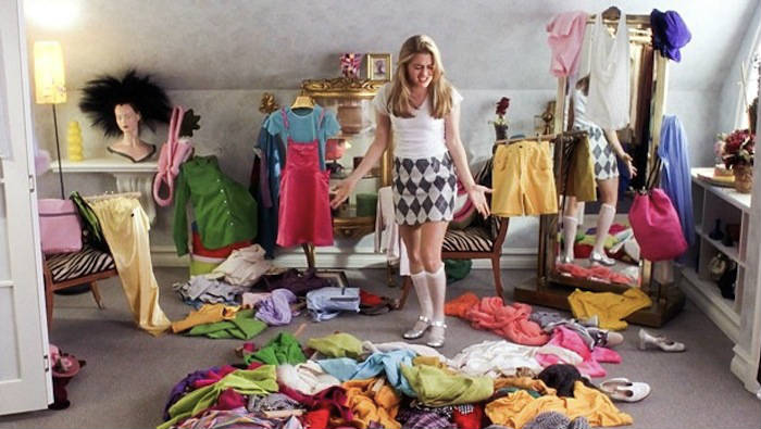 Chica intentando organizar su armario con ropa en el suelo