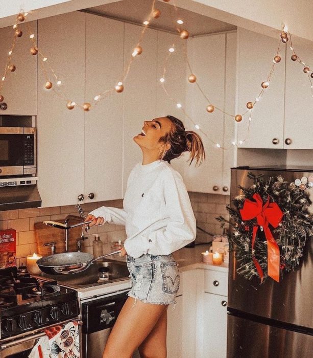 Chica cocinando alegremente en shorts cortos y sudadera blanca
