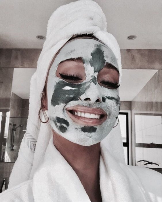 Chica con mascarilla de arcilla y toalla en la cabeza tomando una selfie