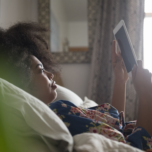 Chica leyendo un texto en su tablet recostada en la cama
