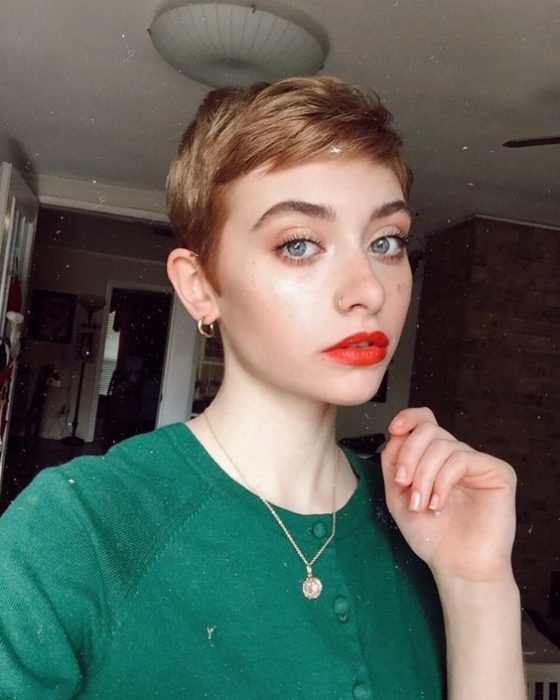 Chica rubia de ojos azules con cabello estilo pixie usa suéter verde