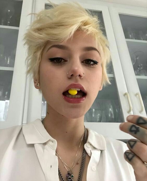 Chica rubia con corte de cabello pixie tiene un dulce amarillo en la boca