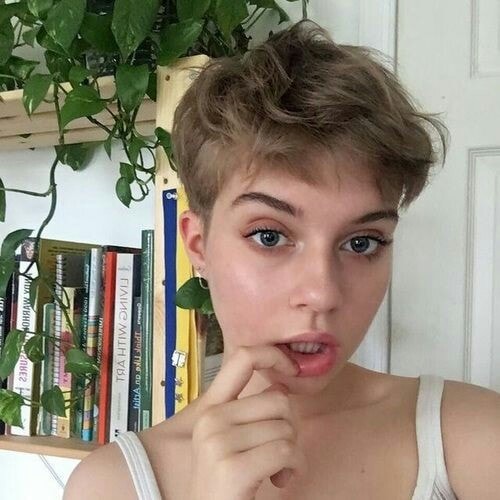 Chica rubia con cabello corto estilo pixie pone su dedo en la boca