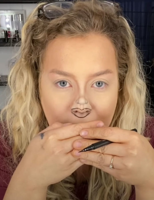 Mujer dibujando labios pequeños sobre su nariz