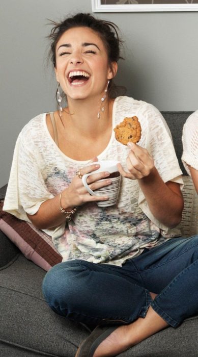 Chica riendo a carcajadas mientras come una galleta y toma un té