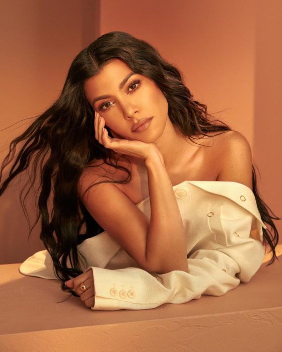Kourtney Kardashian recargada en su brazo con una camisa blanca abierta