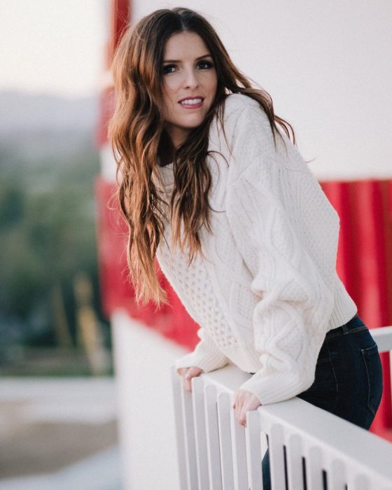 Anna Kendrick apoyada en una barra de madera junto a un puente