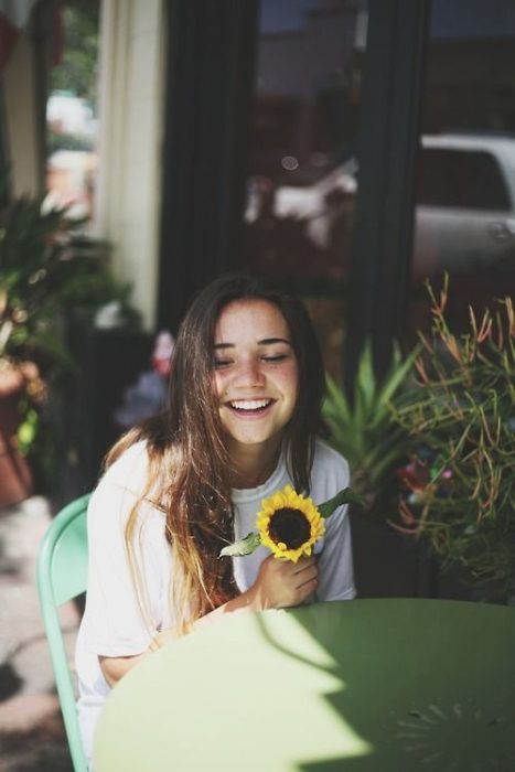 Chica sonriendo sosteniendo un girasol en la mano