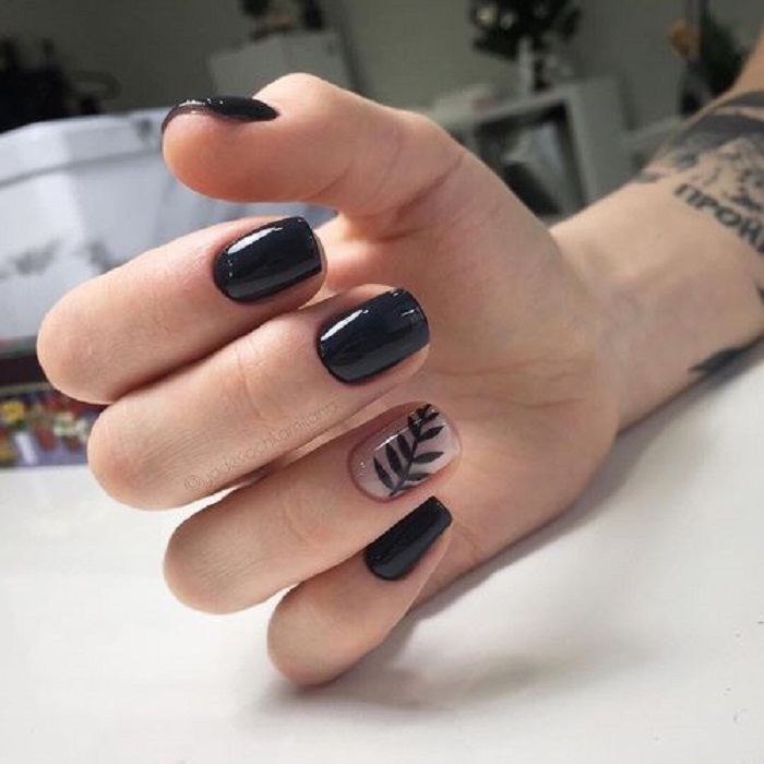 Manicura en color negro con un diseño de hoja en el dedo anular