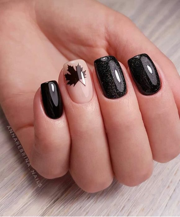 Manicura en color negro con un diseño de hoja de maple en el dedo anular