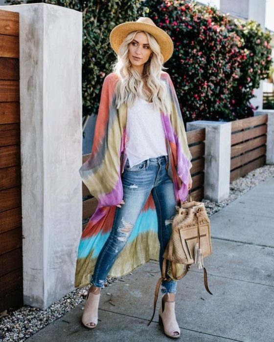Chica rubia posa de pie con un sombrero y un kimono tie dye
