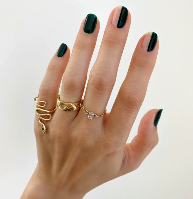 Diseños de uñas sencillos para hacer en casa; esmalte verde oscuro, líneas verticales, mano con anillos dorados de serpiente