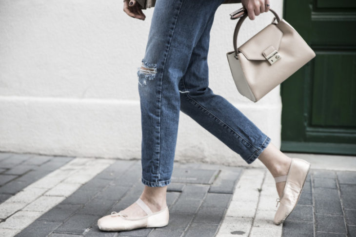 Piernas de mujer van por la calle con jeans y bailarinas rosa palo